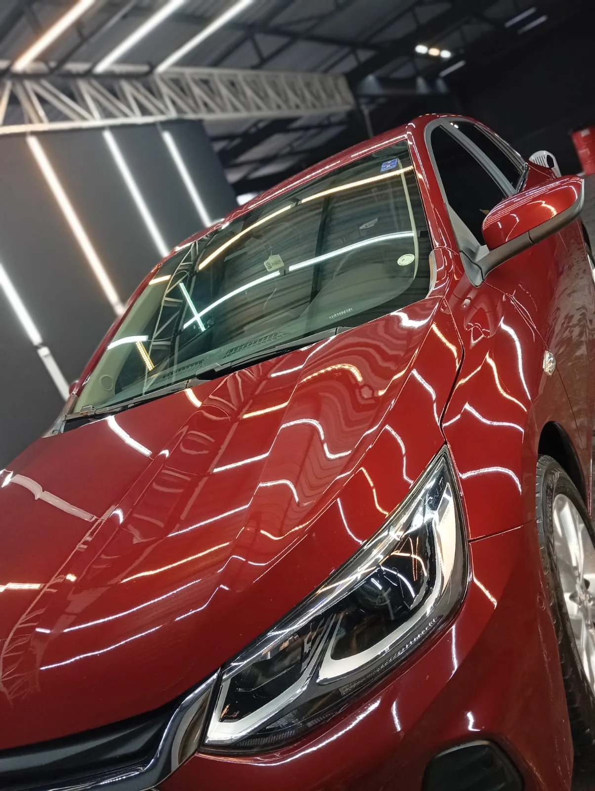 Reflexos das luzes da UNIQUE na pintura de um carro vermelho após o cuidado automotivo